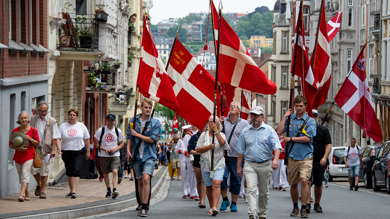 Fahnenträger mit  dänischen Flaggen führen im Juni 2018 einen Umzug durch die Flensburger Innenstadt beim Deutsch-Dänisches Jahrestreffen an.