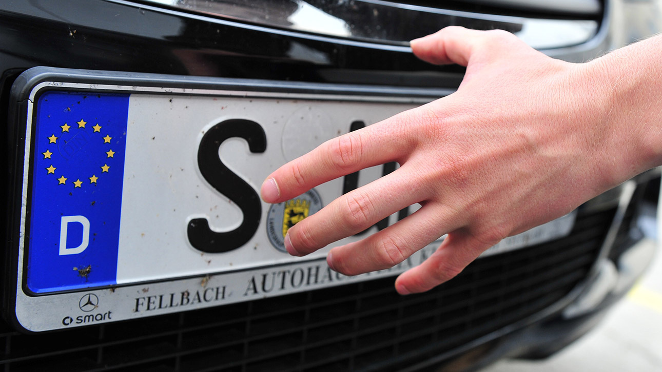 Ein Mann greift nach einem Autokennzeichen an einem Fahrzeug.