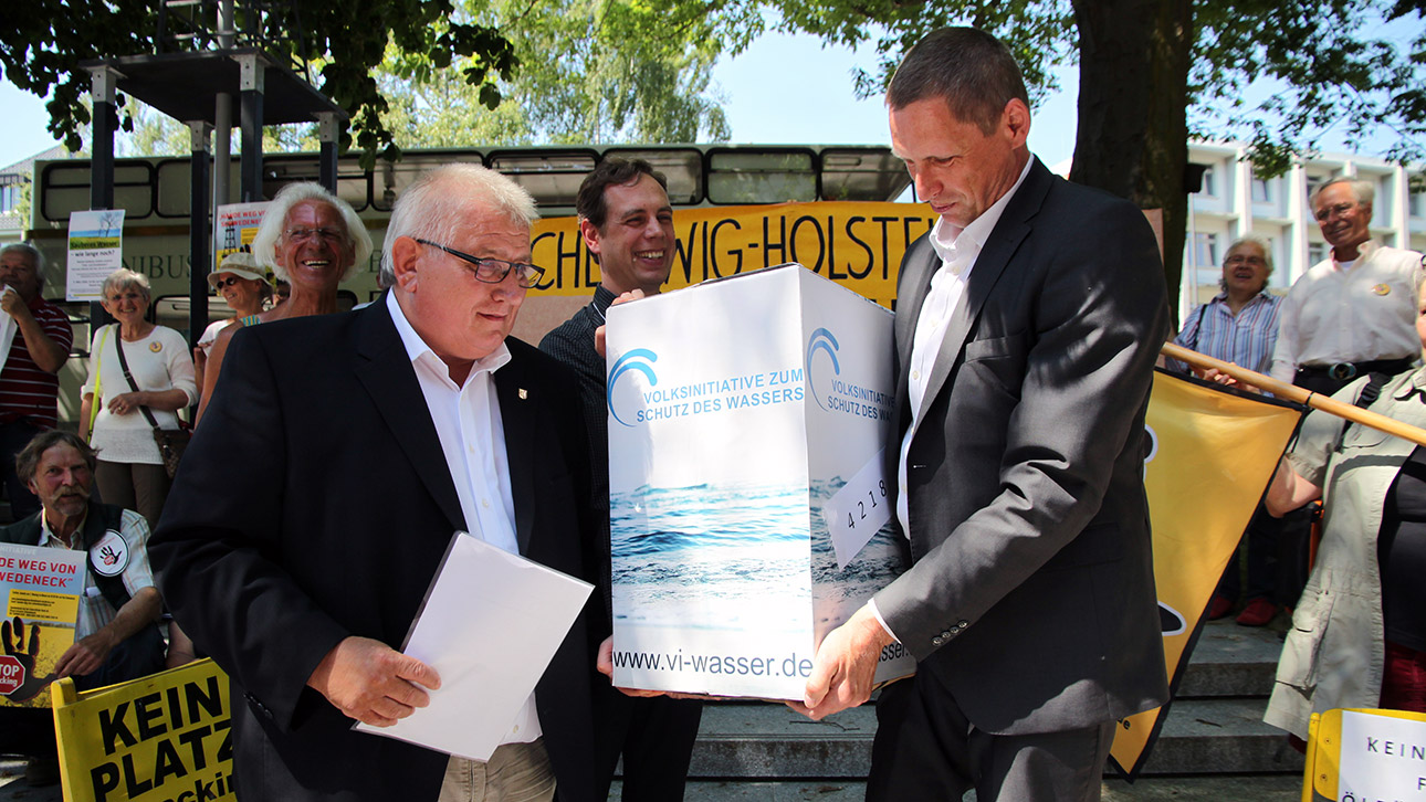 Landtagspräsident Klaus Schlie nimmt eine schwere Kiste mit den gesammelten Unterschriften von Reinhard Knof, Mitinitiator der Volksinitiative zum Schutze des Wasser, in Empfang. 