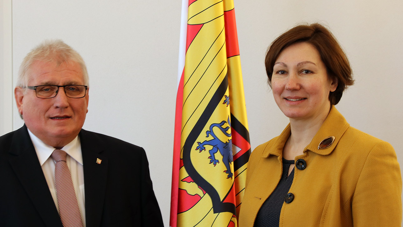 Die Botschafterin der Republik Lettland Skujiņa und Landtagspräsident Schlie stehen neben einer Schleswig-Holstein-Flagge.