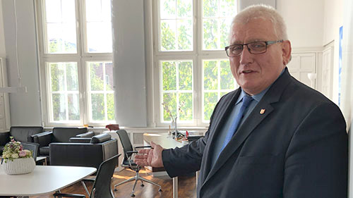 Landtagspräsident Klaus Schlie lädt mit einer Geste in sein Büro ein.