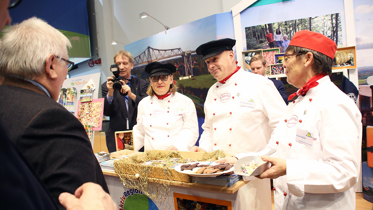 Landtagspräsident Schlie redet mit drei Süßwarenanbieter aus Eckernförde, die ihm Schokolade und Bonbons anbieten.