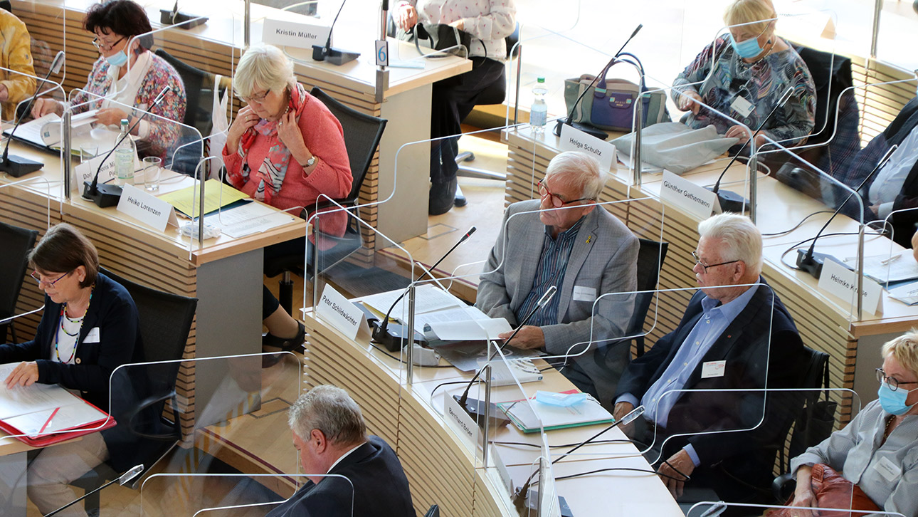 Mitglieder des Altenparlaments im Plenarsaal sitzen hinter Acrylglas-Schutz-Konstruktionen.