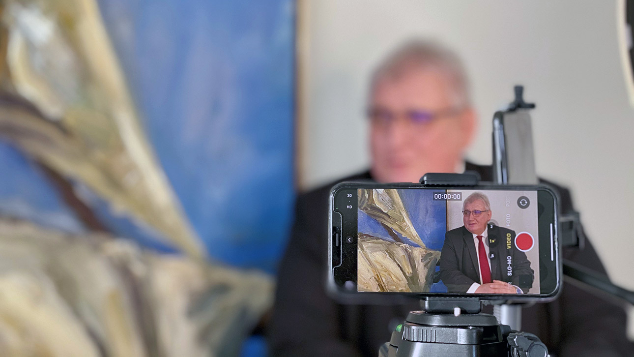 Landtagspräsident Klaus Schlie ist im Vordergrund auf dem Display eines Smartphones zu sehen, der Hintergrund ist verschwommen.