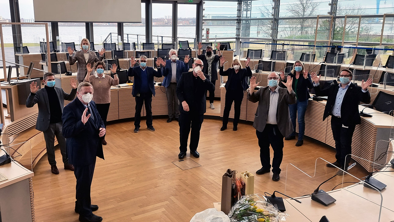 Die Mitglieder des Sozialausschusses und Sozialminister Garg  winken Ulrich Hase im Plenarsaal zum Abschied zu.