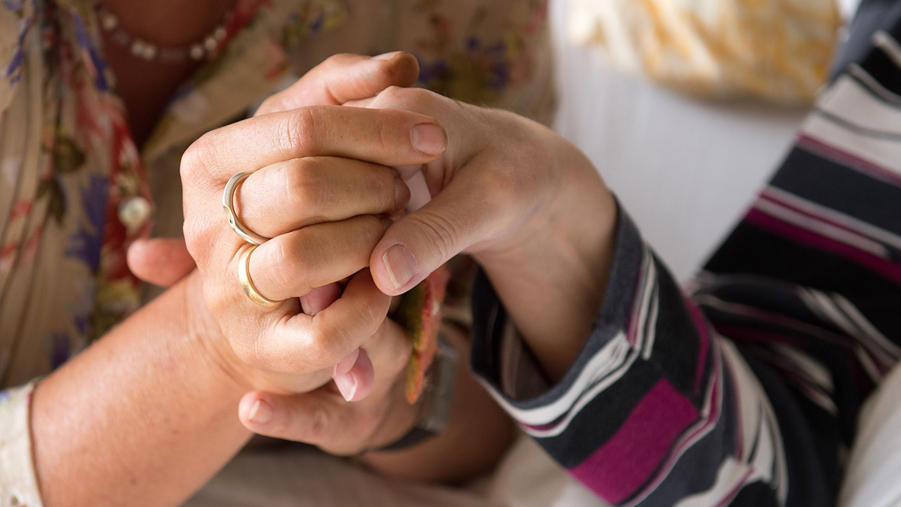 Eine Therapeutin hält in einem Hospiz die Hand einer todkranken Bewohnerin.