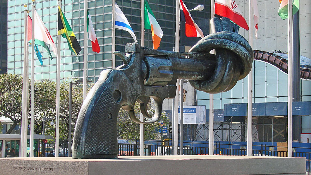 Eine Revolver-Statue mit verknotetem Lauf vor Flaggen verschiedener Staaten