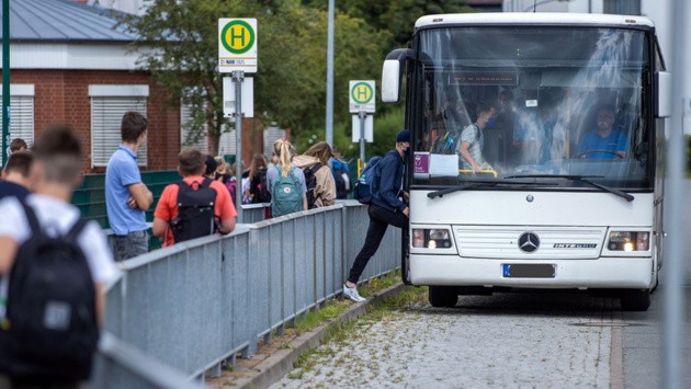 Schüler:innen steigen an einer Bushaltestelle in einen Bus ein.