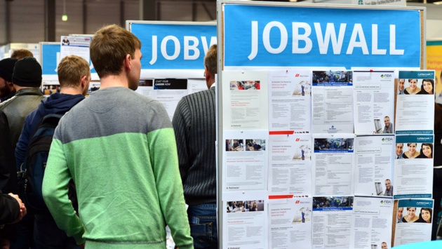  Messebesucher betrachten bei einer Jobmesse Stellenangebote an einer Stellwand.