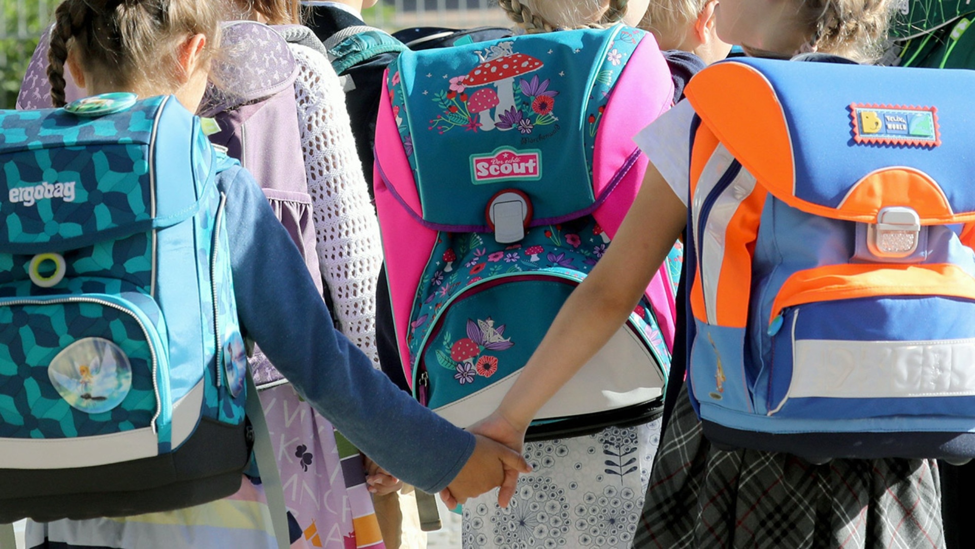 Zwei Mädchen mit Schulranzen gehen Hand in Hand während einer feierlichen Einschulung.