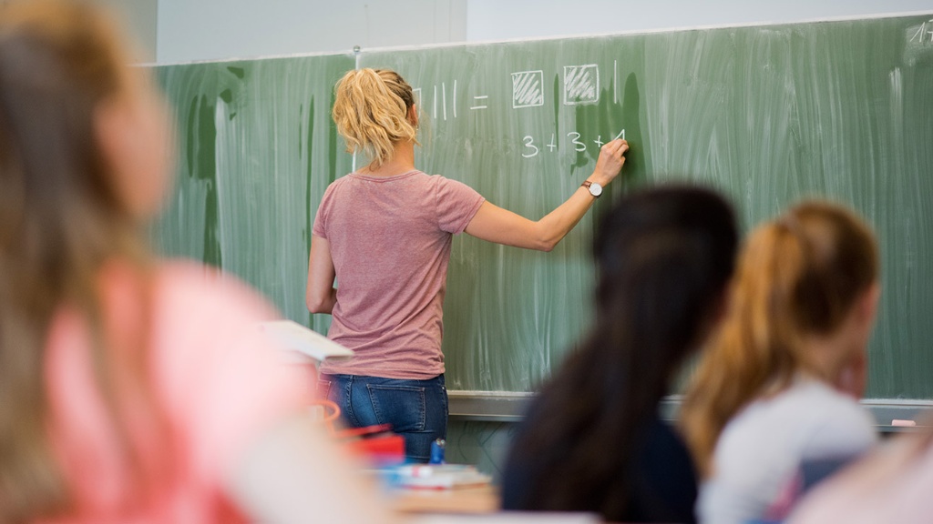 Eine junge Lehrerin schreibt an eine Schultafel im Mathematikunterricht einer achten Klasse an einer weiterführenden Schule. 
