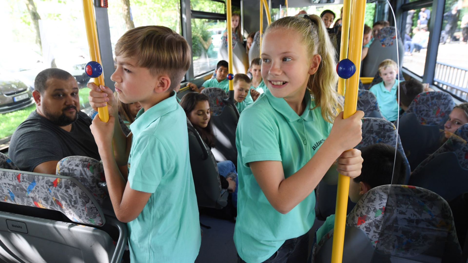 Schüler halten sich während einer Busfahrt an einer Stange fest.