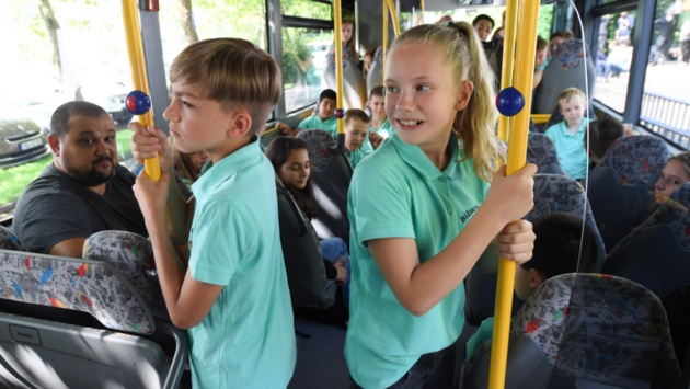 Schüler halten sich während einer Busfahrt an einer Stange fest.