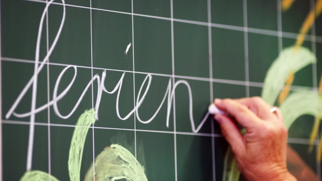 Das Wort "ferien" wird an eine mit Palmen bemalte Schultafel geschrieben.