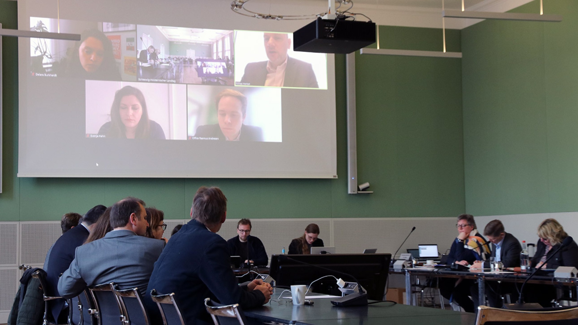 Der Europaausschuss führt mit einigen EU-Parlamentariern, die per Video-Schalte auf Leinwand eingeblendet sind, ein Gespräch. 