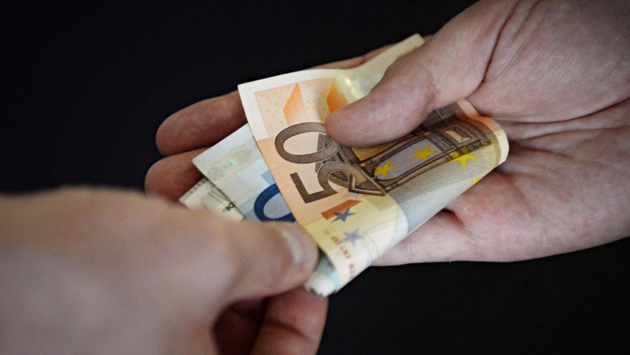 Euroscheine werden von einer Hand in eine andere überreicht.