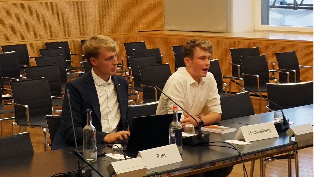 Die Präsidiumsmitglieder von Jugend im Landtag, Lennard Hamelberg und Tim Post sitzen vor Mikrofonen im Ausschusssaal des Landtages.
