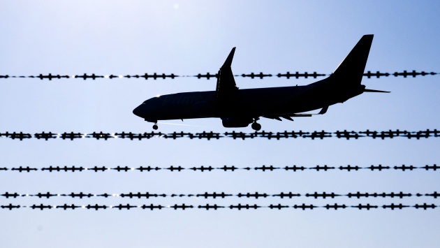Hinter einem Stacheldrahtzaun fliegt ein Flugzeug.
