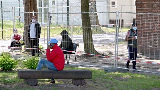 Hinter einem Zaun als Schutzmaßnahme gegen Infektionen sind Flüchtlinge auf dem Gelände des Landesamtes für Zuwanderung und Flüchtlinge zu sehen. 