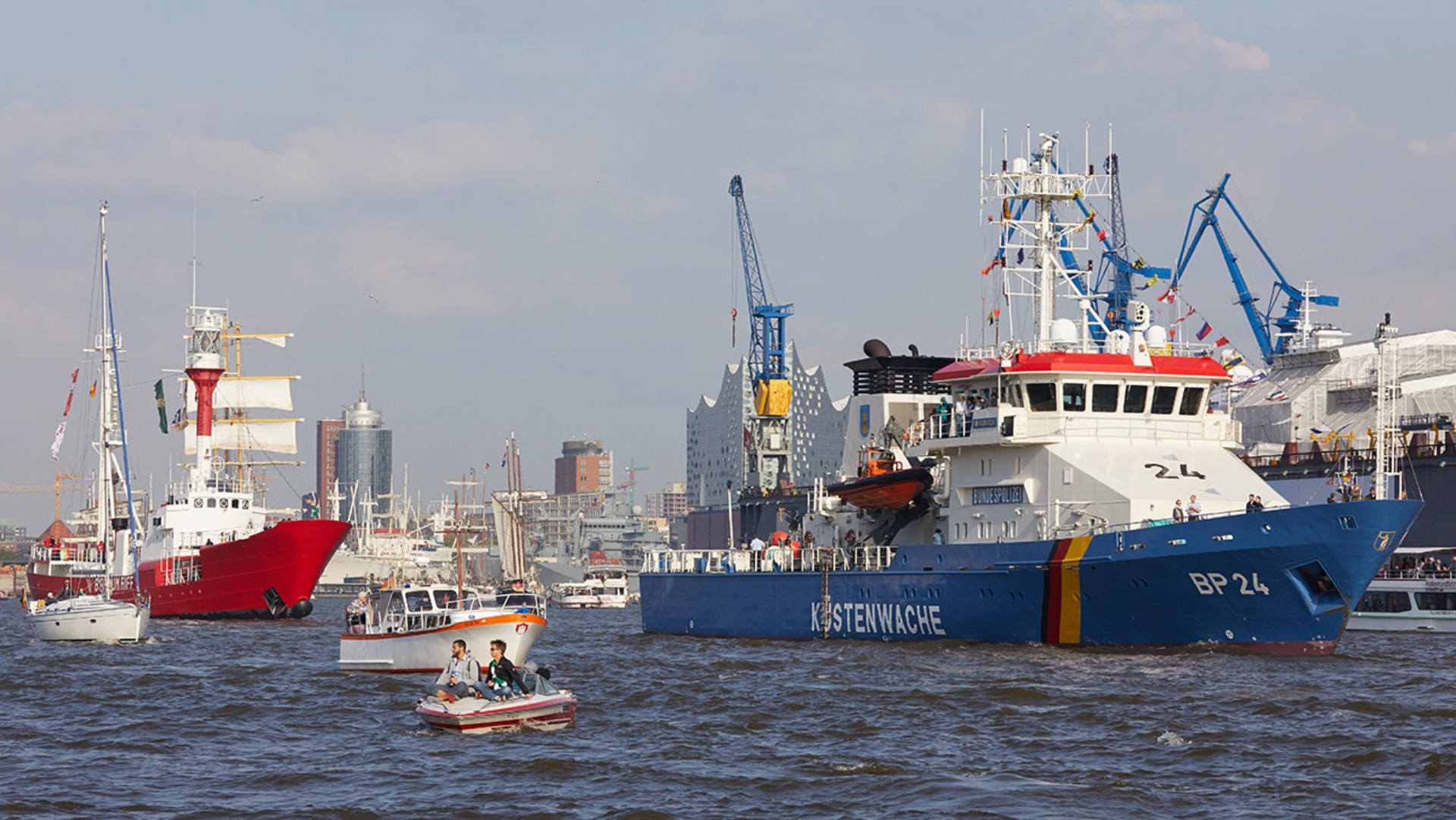Ein Schiff mit der Aufschrift „Küstenwache“ fährt mit anderen Schiffen auf dem Wasser.