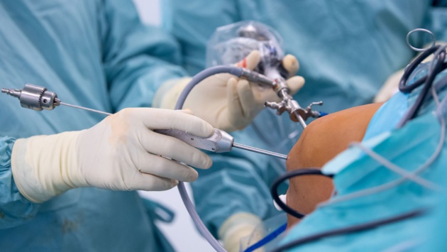 Zwei Hände mit Handschuhen bedeckt führen eine Knieoperation durch.
