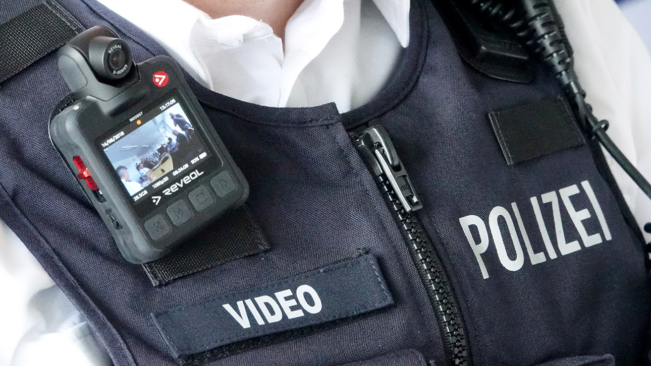 An der Einsatzweste eines Polizisten ist ein Bodycam befestigt.
