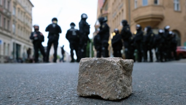 Polizisten stehen auf einer Straße in Leipzig, auf der im Vordergrund ein Pflasterstein liegt.