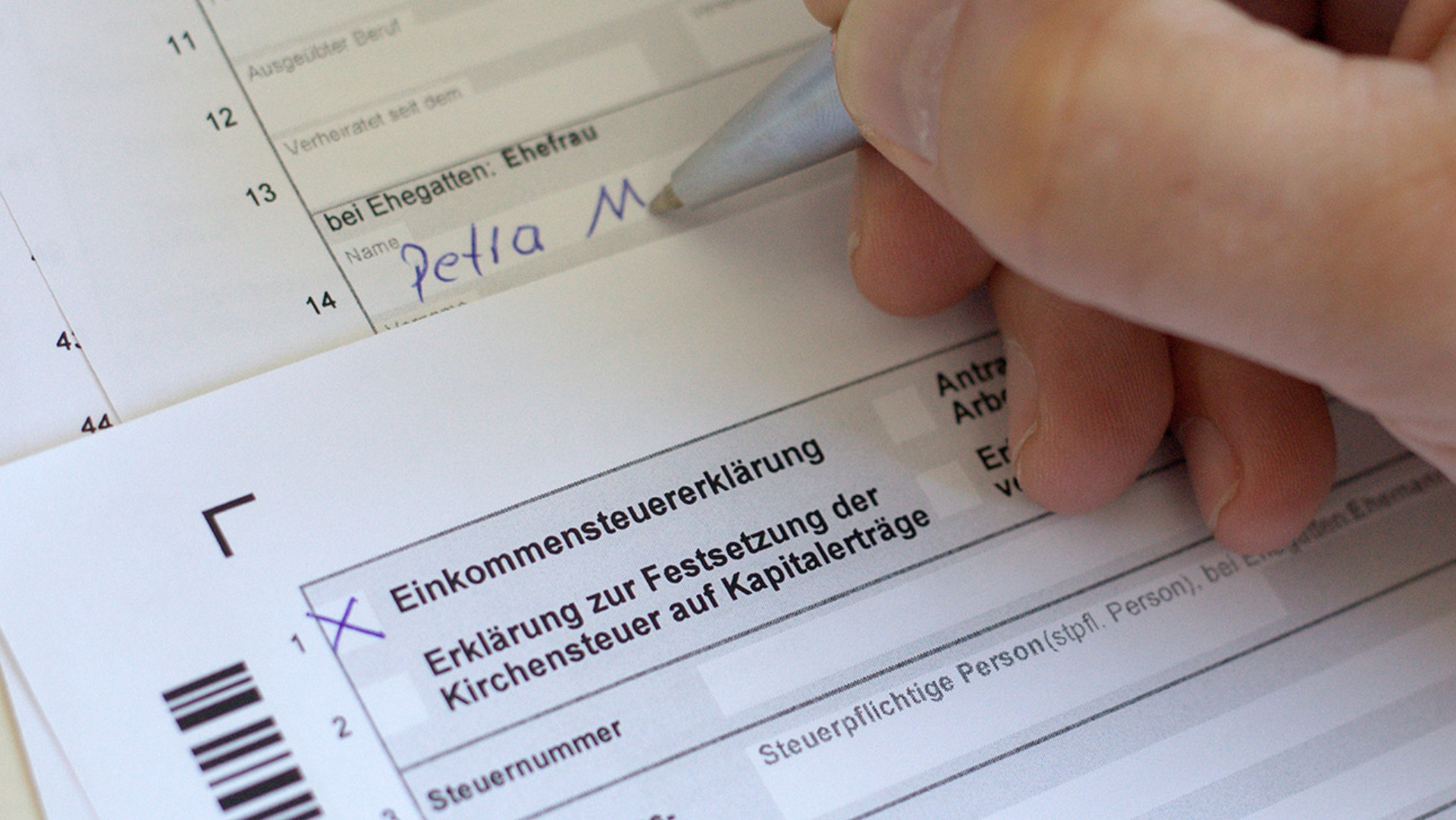 Eine Hand füllt einen Einkommensteuerformular aus.