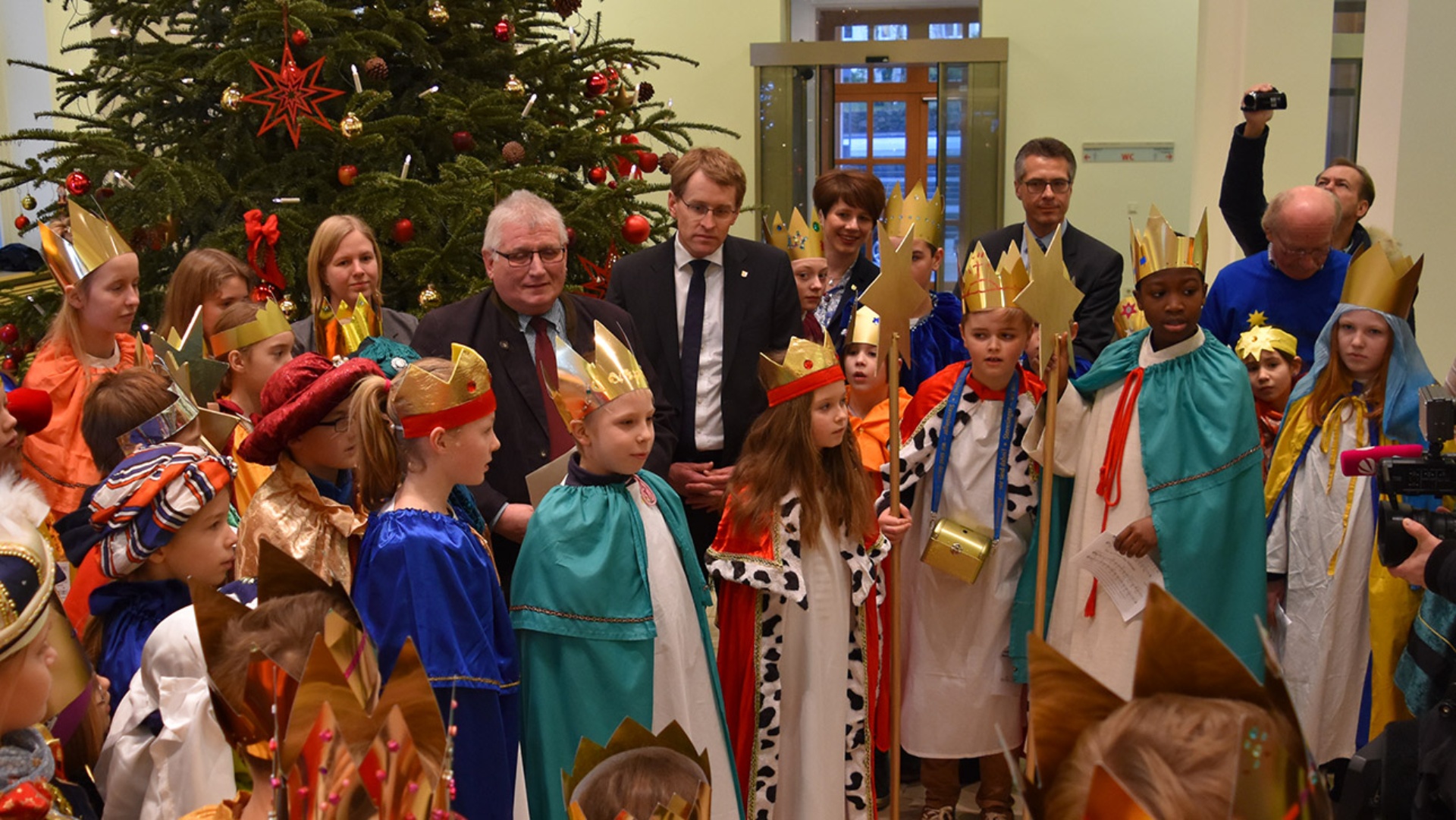 Als Könige verkleidete Kinder stehen zusammen mit Landtagspräsident Klaus Schlie und Ministerpräsident Daniel Günther in der Eingangshalle des Landeshauses.