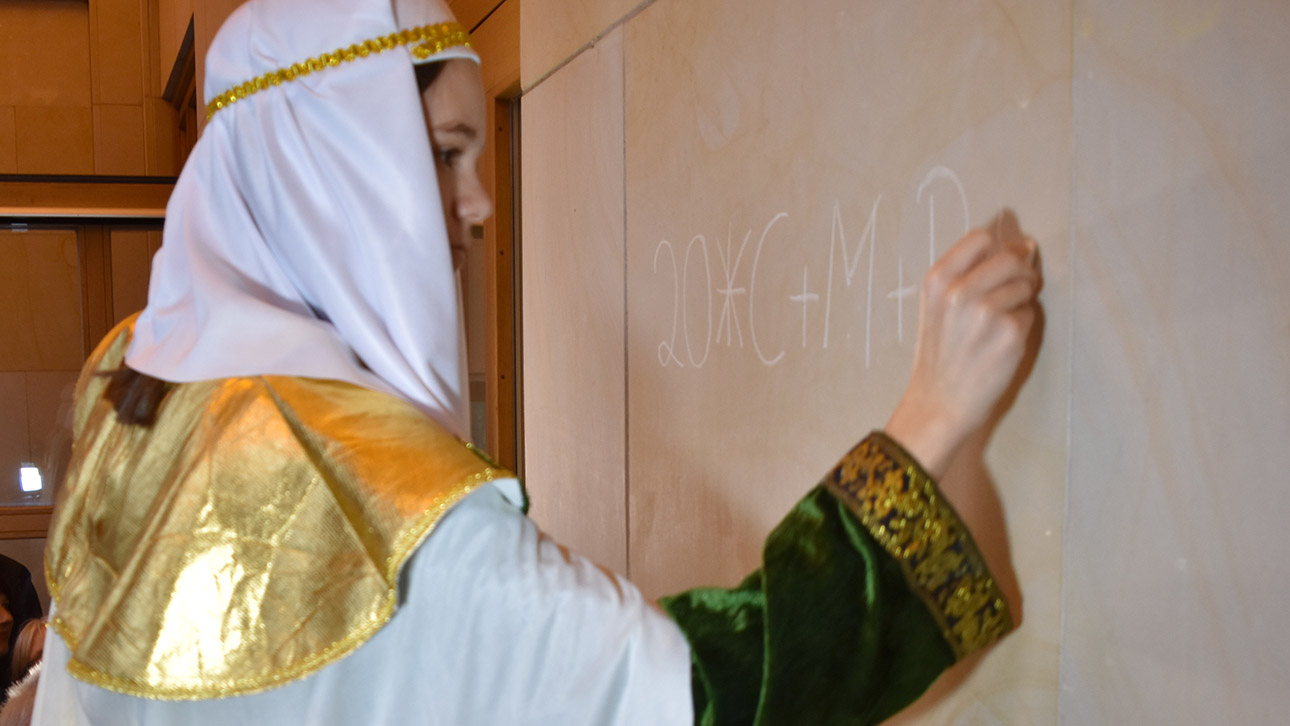 Ein kostümiertes Mädchen schreibt 20*C+M+B+18 mit Kreide an die Hauswand des Landtages.