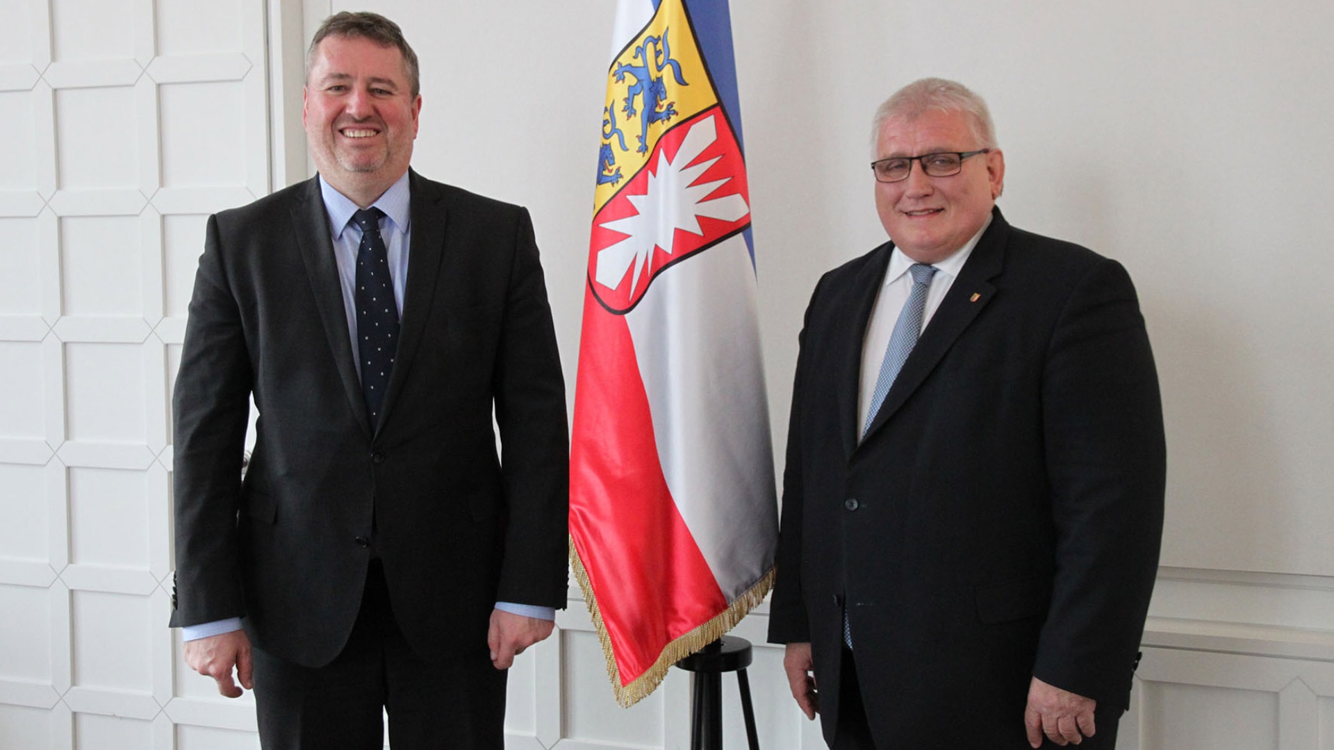 Der Ungarische Botschafter, Péter Györkös, und Landtagspräsident Klaus Schlie stehen vor der Schleswig-Holstein-Fahne.