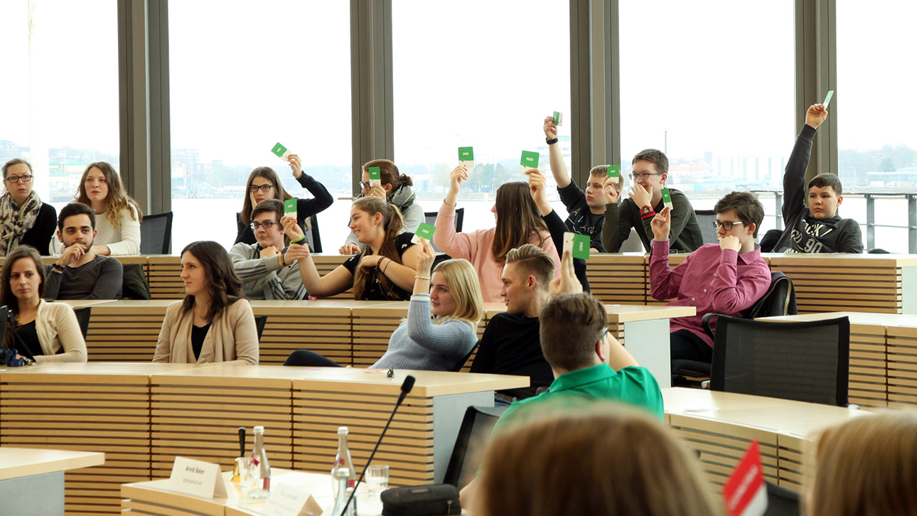Jugendliche sitzen im Plenarsaal und halten rote und grüne Karten hoch.