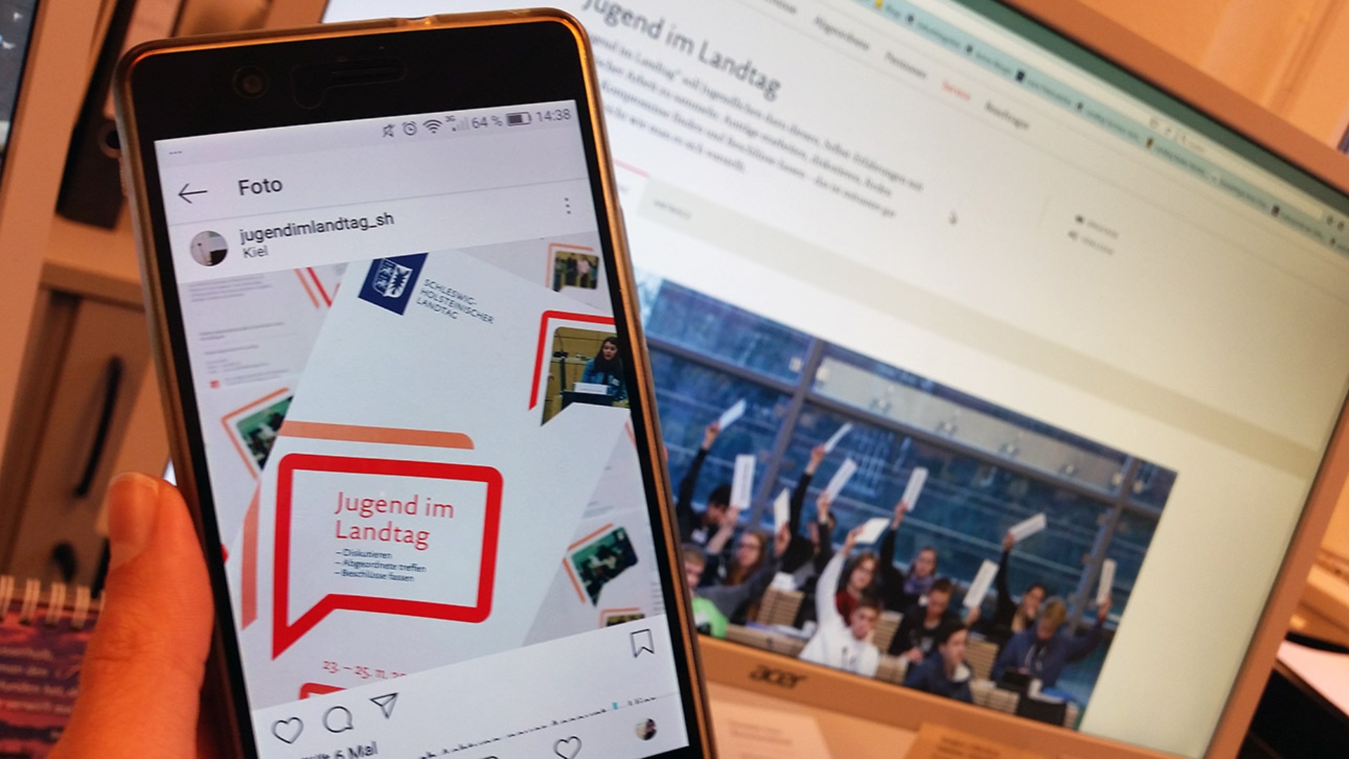 Auf einem Handy ist das Logo von Jugend im Landtag auf Instagram zu sehen. Im Hintergrund: Ein Bild von Jugendlichen auf einem Loptop.