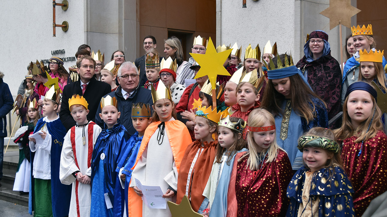 Gruppenfoto: Die bunt verkleideten Sternsinger stehen nach ihrer Ankunft mit Landtagspräsident Klaus Schlie und Ministerpräsident Daniel Günther vor dem Landeshaus.