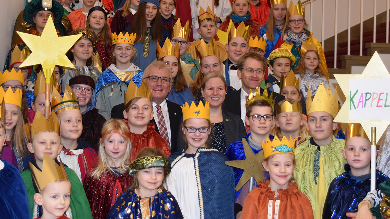 Gruppenfoto der Sternsinger mit Landtagspräsident Schlie und Ministerpräsident Günther auf einer Treppe in der Eingangshalle des Landeshauses.