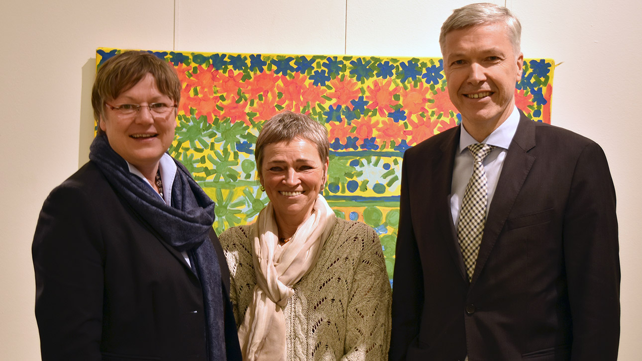 Drei Menschen posieren vor einem Bild in der Ausstellung.