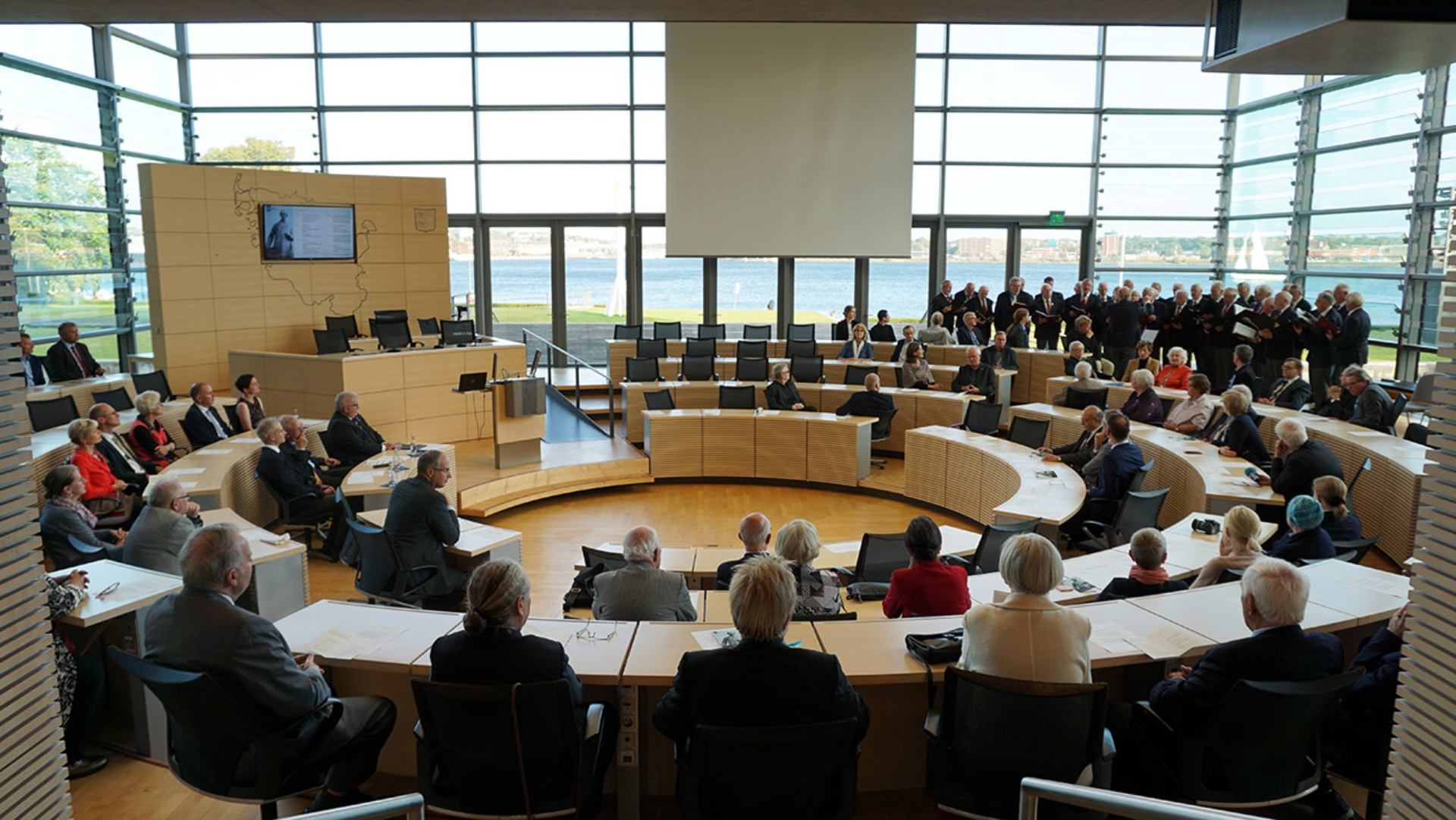 Rund 100 Gäste sitzen im Rund des Plenarsaals und lauschen dem Gesang des Heider Männerchors von 1841.