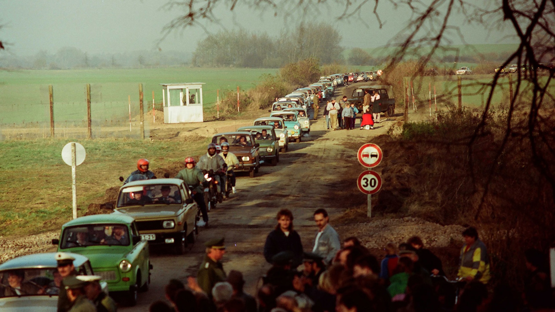 Schlangen von Trabis, die unter den Augen des Bundesgrenzschutzes und des Zolls in Richtung Westen fahren.