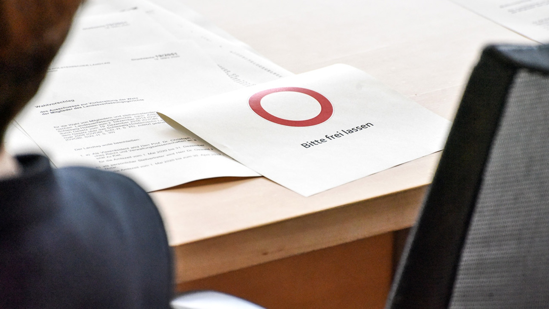 Ein Zettel mit dem Hinweis "Bitte freilassen" auf einem Abgeordnetenplatz im Plenarsaal