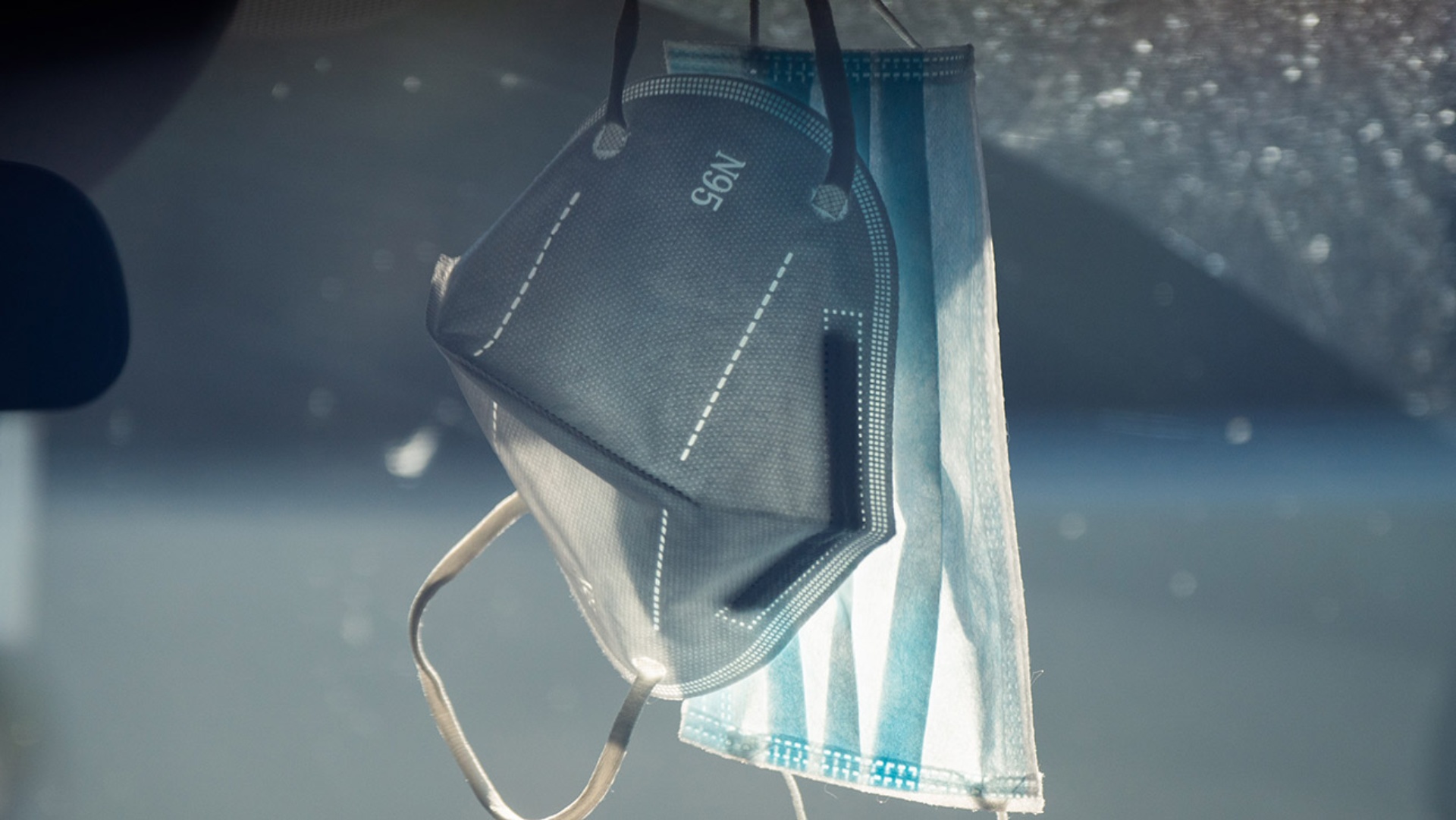 Zwei Schutzmasken hängen vor einer Scheibe.