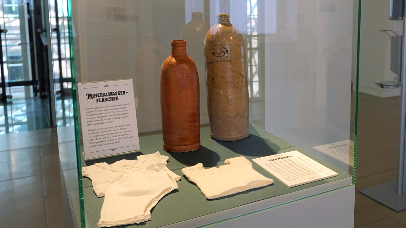 Blick auf einen Glaskasten in der Ausstellung zum Thema Seebäder mit alten Wasserflaschen aus Ton.