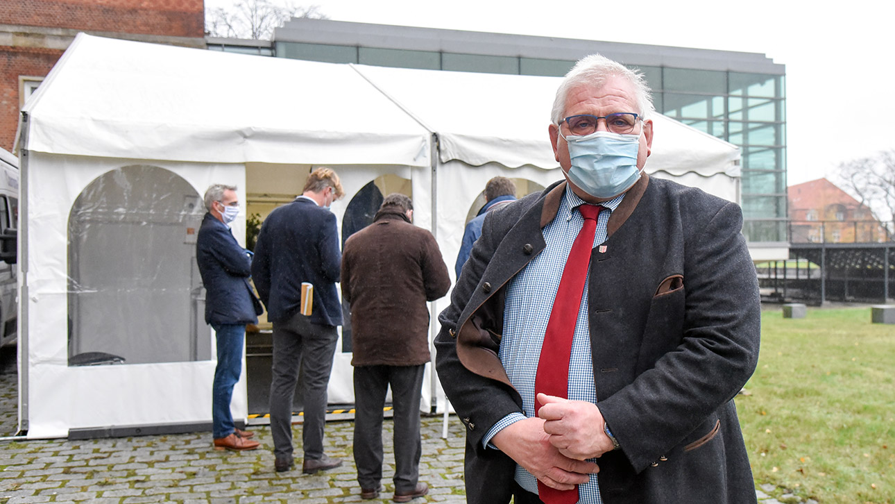 Landtagspräsident Klaus Schlie steht mit Mund-/Nasenschutz vor einer mobilen Teststation. im Hintergrund ist der Plenarsaal.