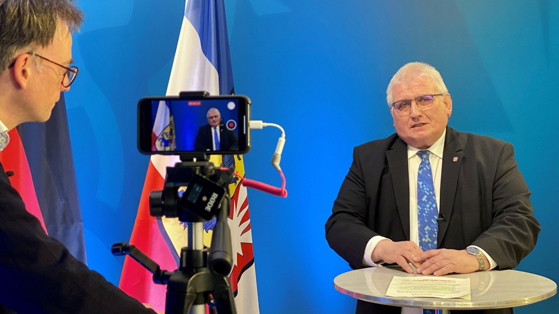 Landtagspräsident Klaus Schlie antwortet auf eine Frage von Jan Schlürmann. Auf einem Stativ ist ein Smartphone, das das Gespräch aufzeichnet.