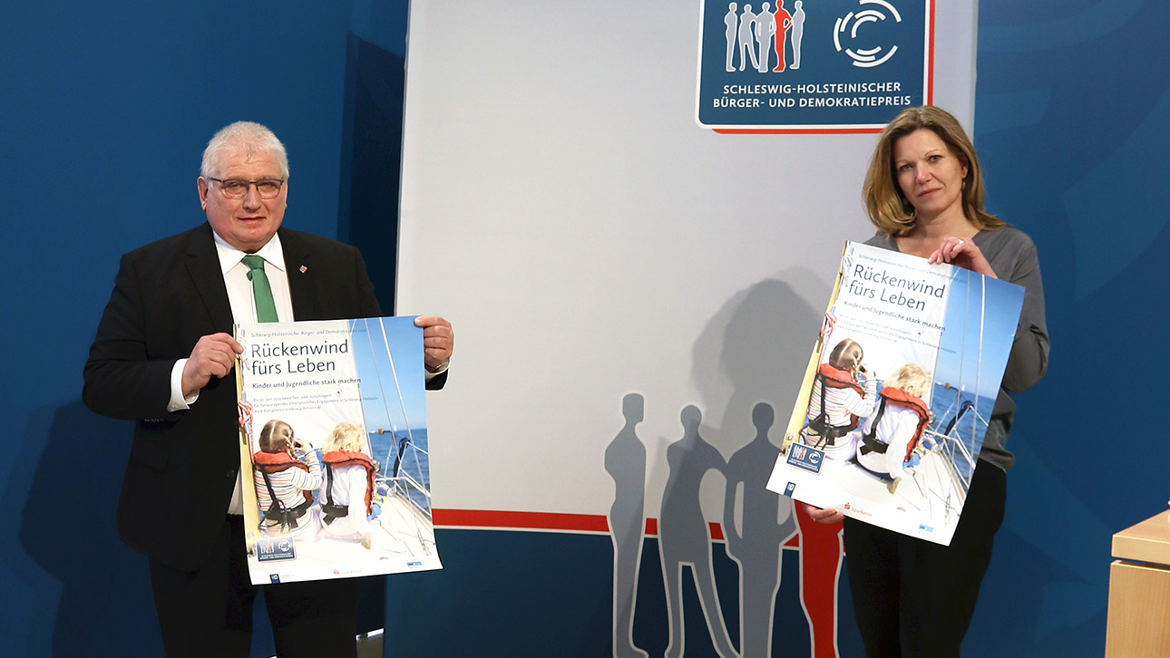 Landtagspräsident Klaus Schlie und Gyde Opitz vom Sparkassenverband stellen das Motto des Bürgerpreises vor. Beide halten Plakate in den Händen.