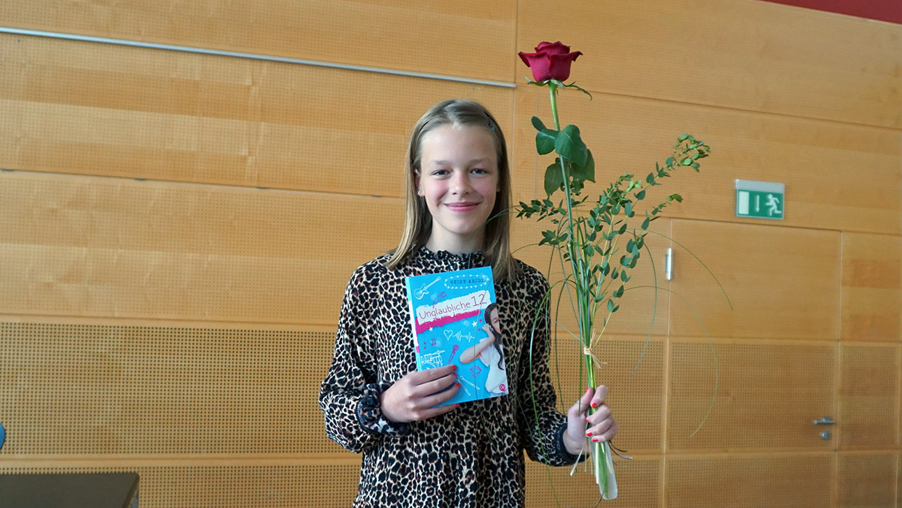 Emilie Wunderlich freut sich mit Buch und roter Rose in den Händen über ihren Sieg im Vorlesewettbewerb.