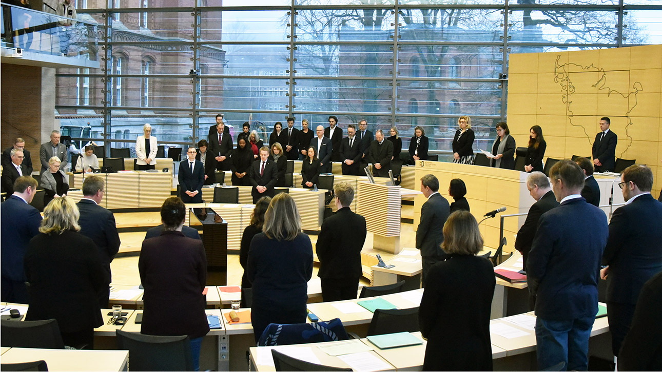 Stehend gedenken die Abgeordneten im Plenarsaal der Opfer der Zugattacke von Brokstedt.