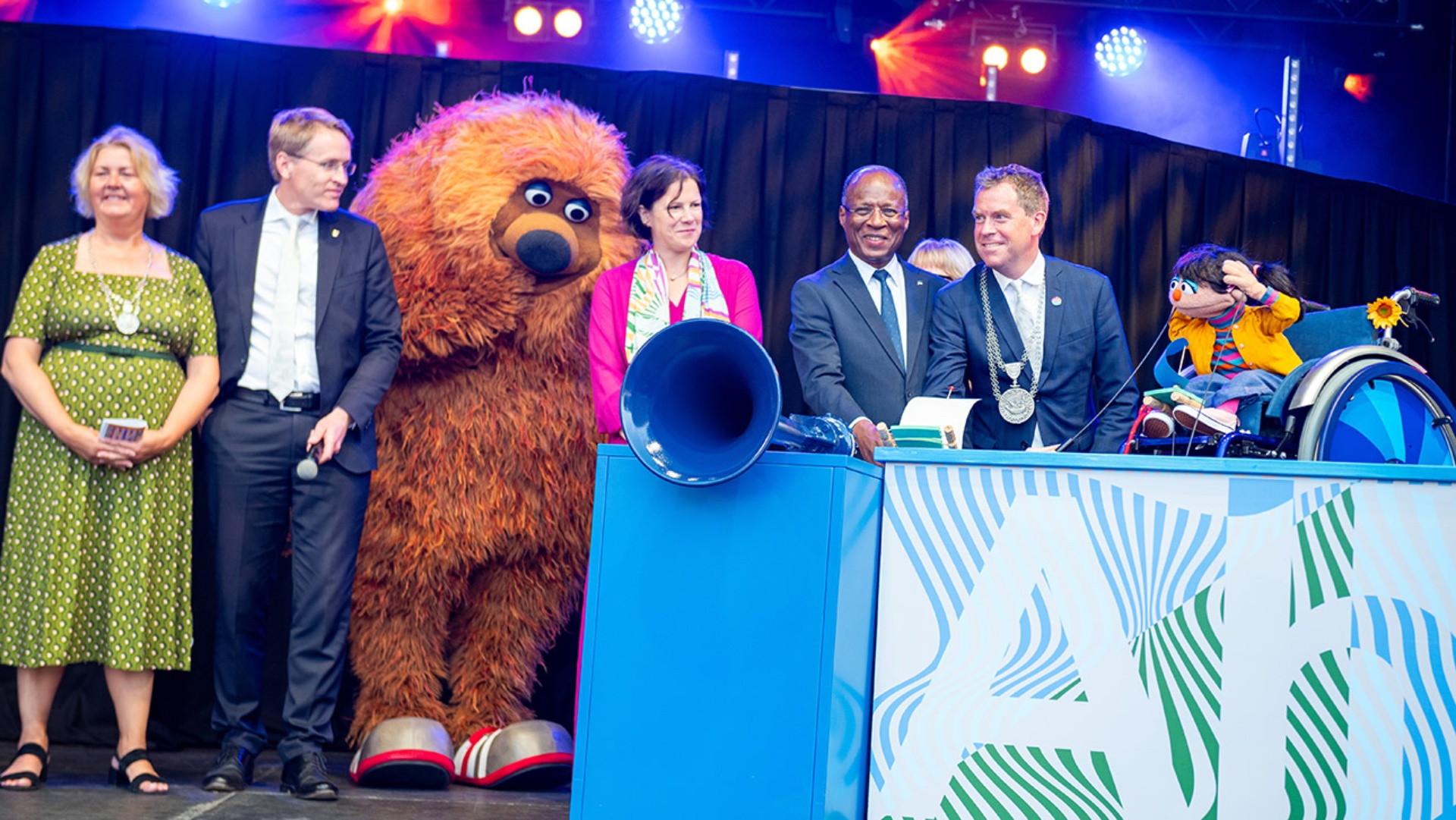 Landtagspräsidentin Kristina Herbst (4.v.l), Ministerpräsident Daniel Günther (CDU, 2.v.l), José Ulisses de Pina Correia e Silva (3.v.r), Premierminister des westafrikanischen Inselstaates Kap Verde, Kiels Oberbürgermeister Ulf Kämpfer (SPD, 2.v.r), Kiels Stadtpräsidentin Bettina Aust (l.) sowie Samson (3.v.r.) und Elin (r.) aus der "Sesamstraße" eröffnen mit dem Schiffshorn die Kieler Woche. 