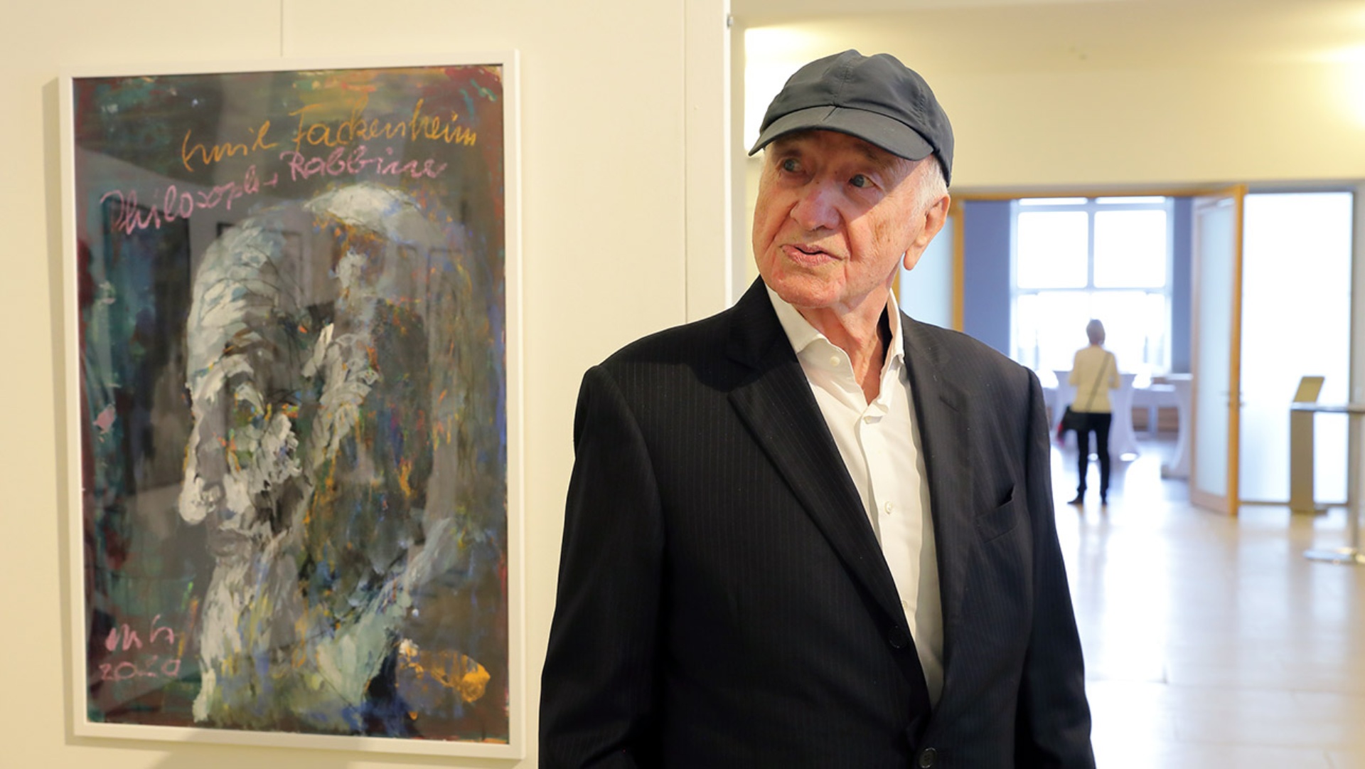 Armin Mueller-Stahl steht bei der Vernissage vor einem seiner Bilder. Er trägt eine dunkle Schirmmütze.