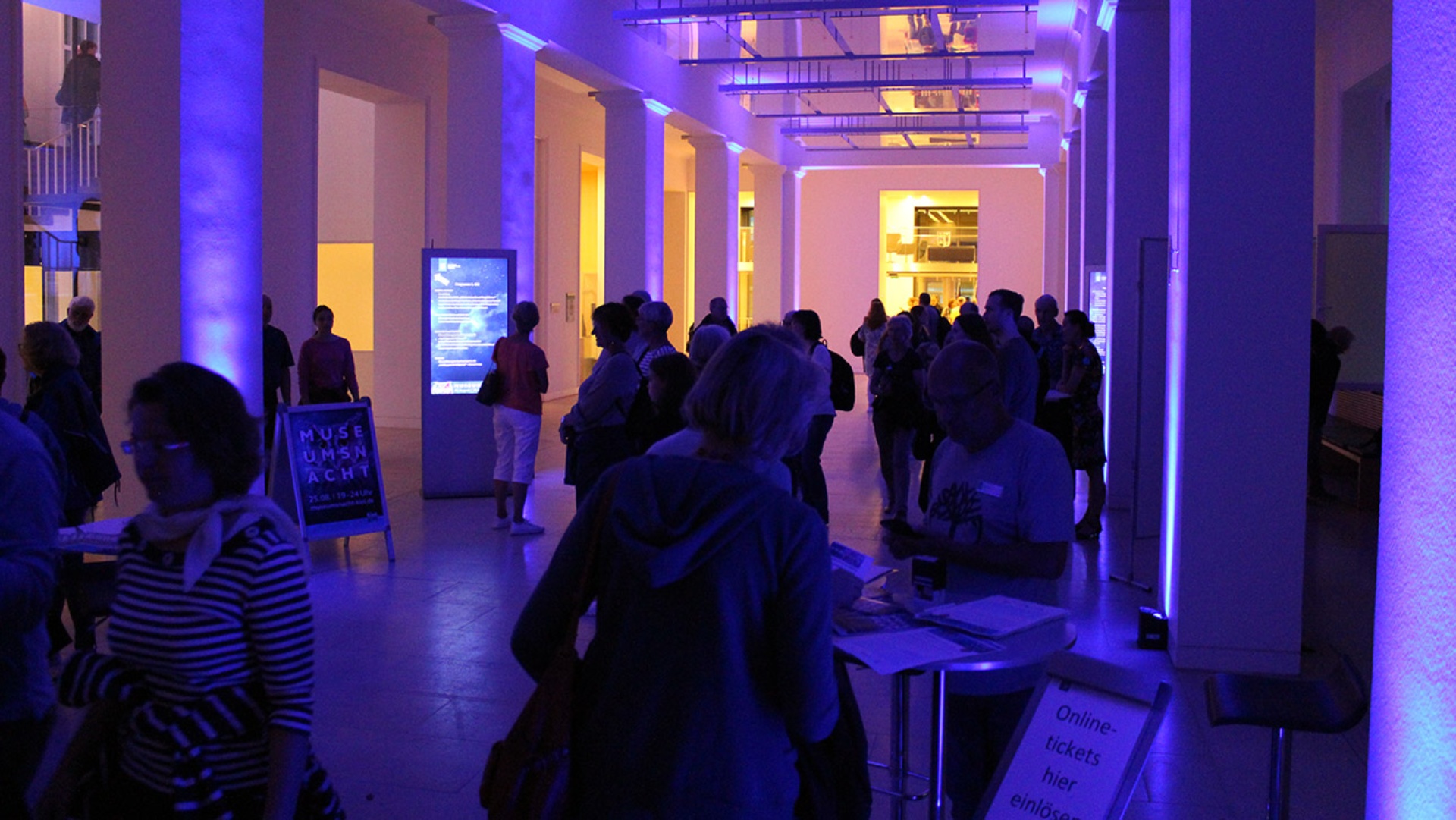 Die Eingangshalle des Landeshauses, die mit zahlreichen Gäste gefüllt ist, ist in violettes Licht getaucht.