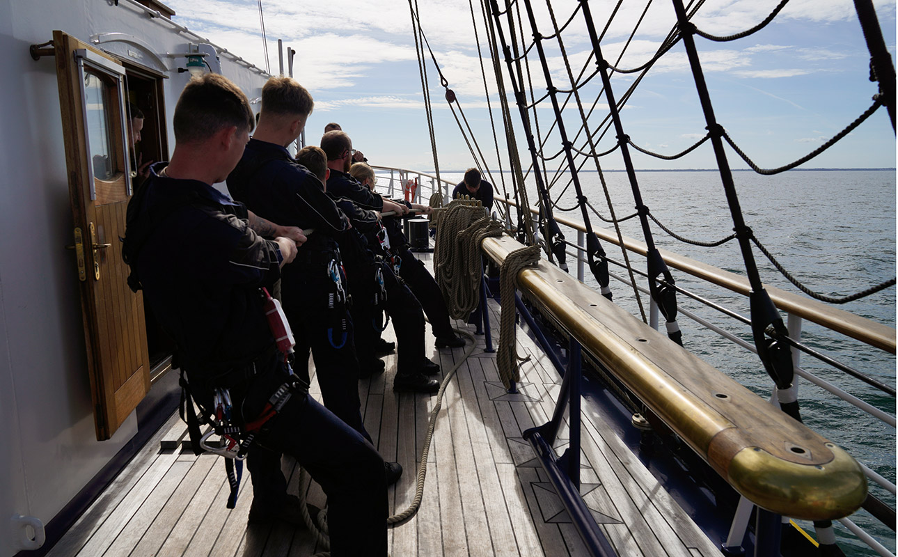 Mit vereinten Kräften ziehen Crew-Mitglieder an den Leinen beim Segel-Setzen